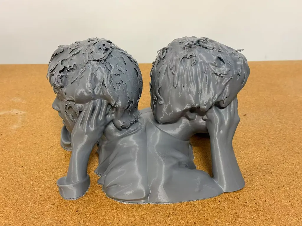 灰色3D打印双人半身像，两个头向外转，置于软木表面，从背面拍摄。