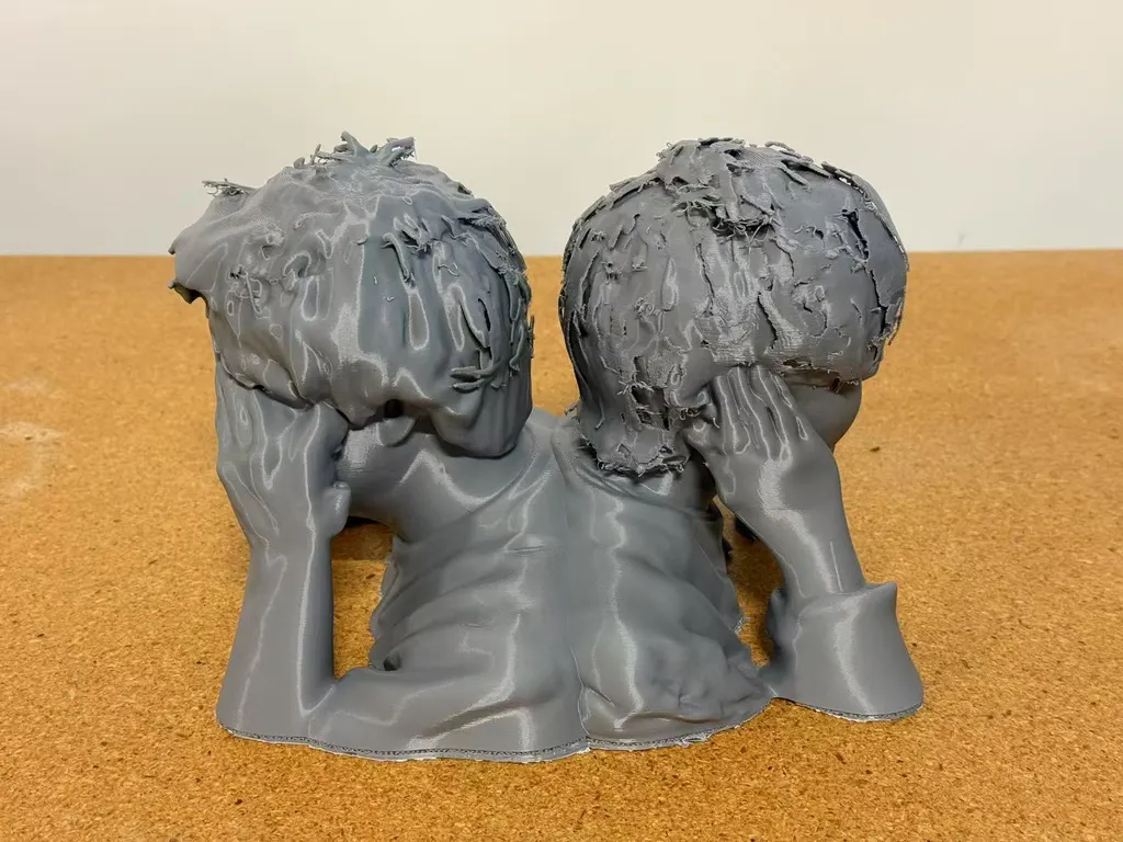 灰色3D打印双人半身像背面，可见两个头和抬起的手，置于软木表面。