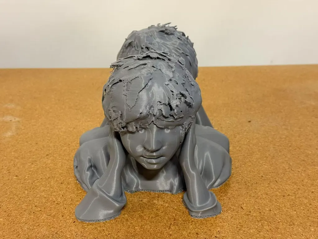 灰色3D打印双人半身像正面，前方头部夹在双手之间，置于软木表面。