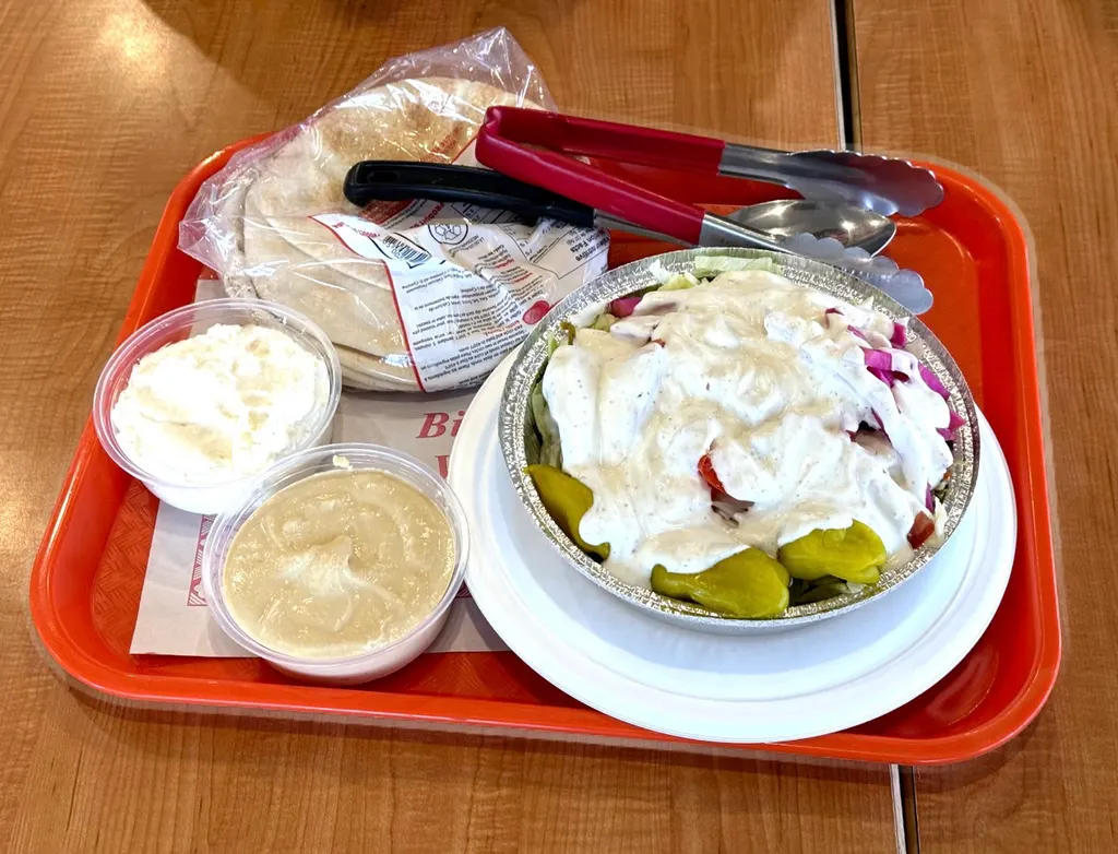 橙色托盘上有皮塔饼、夹子、鹰嘴豆泥、白色蘸酱和覆白酱的沙拉碗。