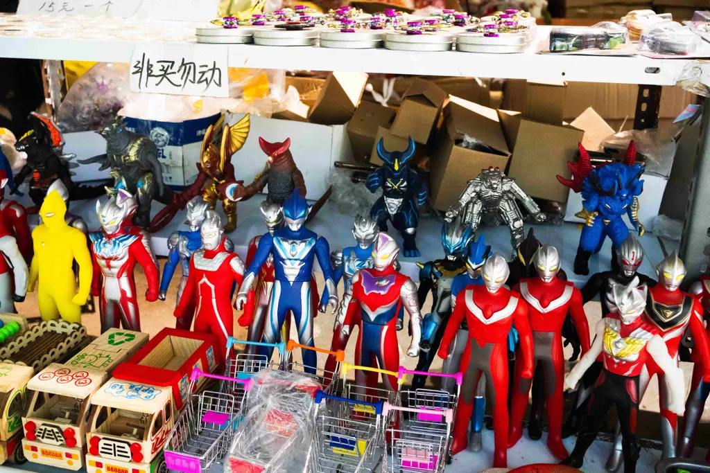 Toy figures and carts are displayed on a market shelf under handwritten Chinese signs.
