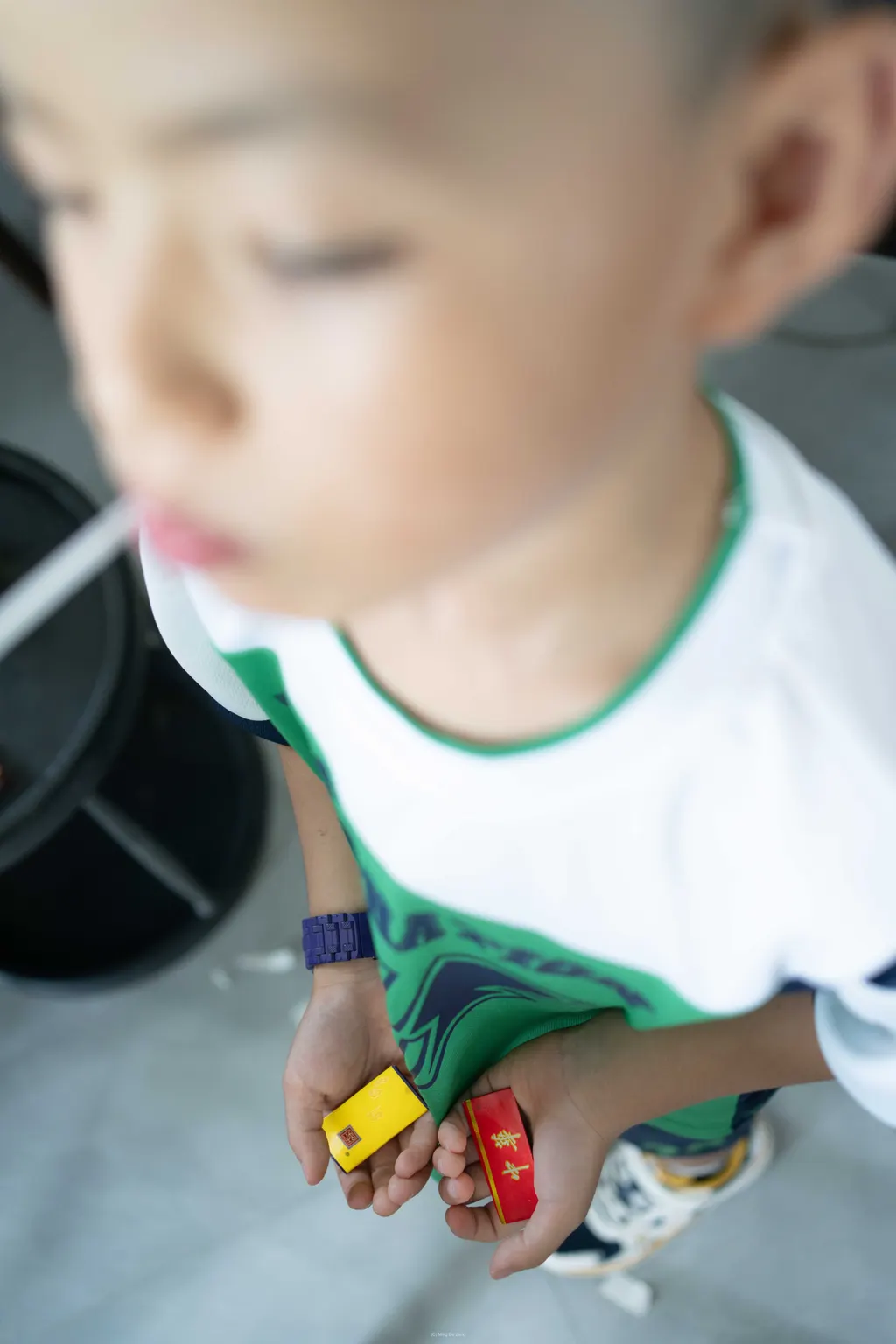 Blurred close-up of a child's face and torso, with hands holding small rectangular pieces.