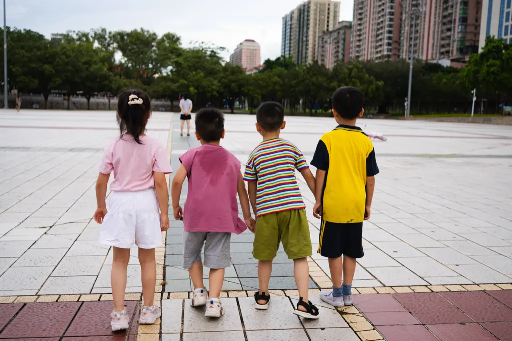 Four children stand with backs to the camera on a tiled plaza facing a distant adult.