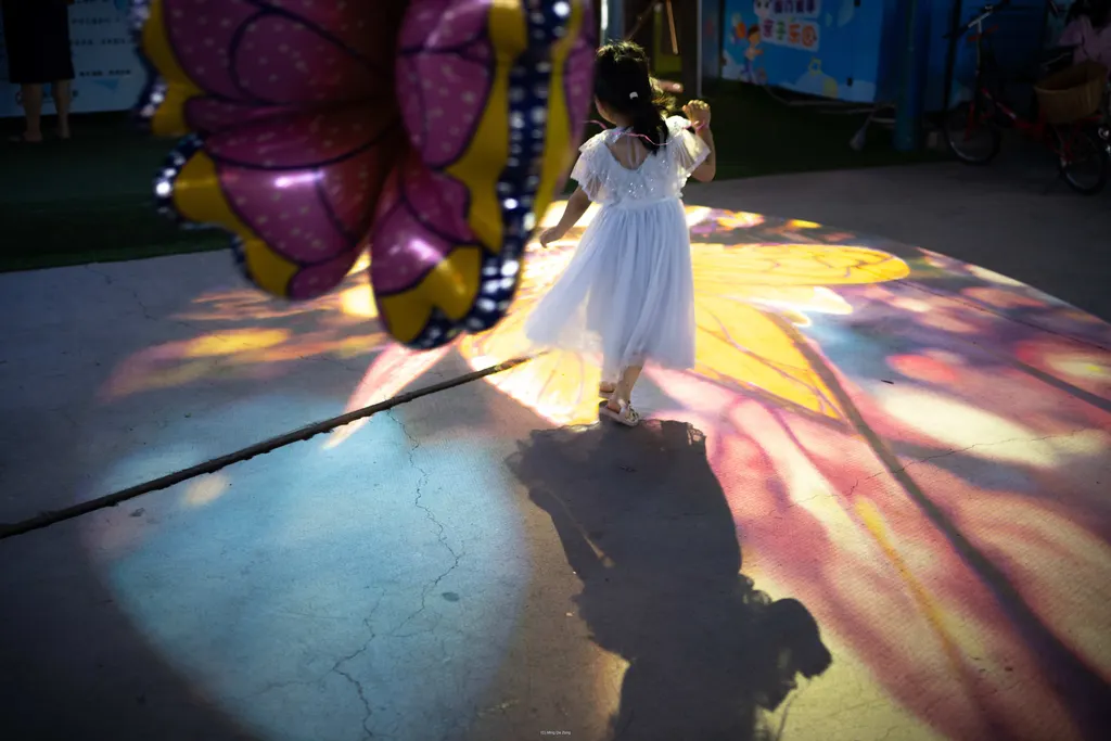 Girl in a white dress walks through projected butterfly light on a dark floor.