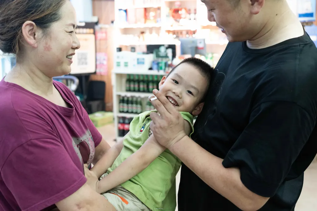 Two adults hold a smiling boy in a shop; one adult's hand holds a cigarette near his face.