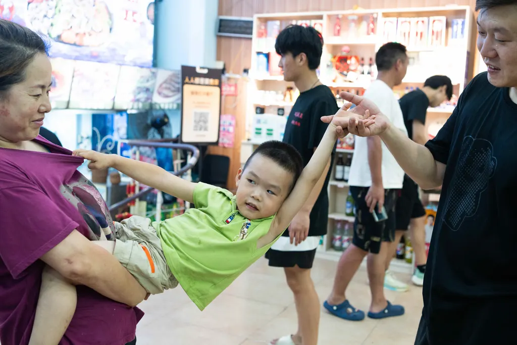Boy is held between two adults in a shop, reaching toward a woman's shirt.