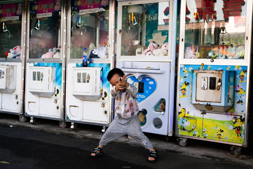 Boy poses with a toy gun in front of claw machines filled with plush toys.