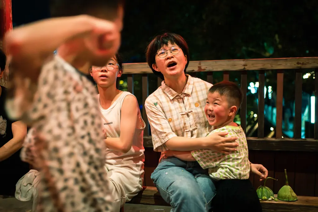 Night scene of adults and children sitting on a bench, with one child blurred in foreground.